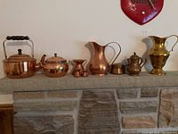 Full view of all copper and brass items arranged on stone mantle, showing kettle, jugs and pots