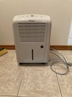Front view of white Danby Premiere dehumidifier showing air vent and connected power cord on tiled floor.
