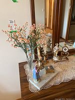 Wide view of all decor items arranged on lace runner on table showing flowers, candlesticks, figurines, clock, and trinket box