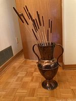 Copper floor vase standing on hardwood floor with bulrushes inside.