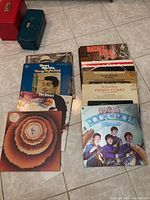 Top-down view of LP records stacked on floor showing multiple vintage album covers including The Beatles, The Doors, Elton John, Perry Como, Stevie Wonder.