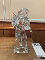 Side view of clear crystal angel violin figurine on wood surface, showing detail of the angel holding violin.