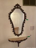 Full view of the ornate framed wall mirror hanging above matching wall shelf