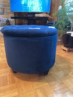 Side view showing round shape, blue velvety upholstery, and tufted top with buttons.