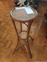 Rattan plant stand viewed from a low angle showing top surface and leg structure on parquet flooring.