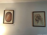 Two framed art prints on wall: left shows profile of a human head, right shows a woman's face in profile with curly hair, both in wood gilt frames.