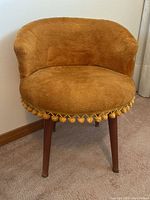 Front view of the retro upholstered chair showing the plush orange fabric, rounded seat and pom-pom trim.