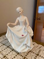 Front and left side view of the Royal Doulton 'Tracy' figurine showing the pose holding the dress and pink flower detail.