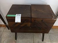 Front view of the dark wood accordion sewing box closed showing broken top right corner and metal hinge supports.