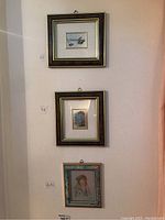 Three framed wall art pieces on a white wall, including a boat scene, a tree, and a floral portrait.