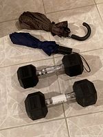 Photo showing 2 dumbbells and 2 foldable umbrellas on tiled floor, side view
