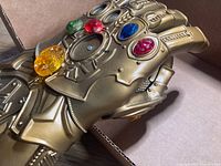 Close up photo of a gold-colored Thanos gauntlet with six colored gems attached, showing details of the stones and gauntlet design.