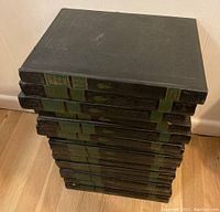 Stack of 15 dark green hardcover books showing spines with gold and green labels, embossed details on cover and spines, showing complete set thickness and condition.