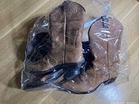 Photo showing two pairs of vintage cowboy boots in light and darker brown colors, placed side by side with one pair inside a plastic bag.