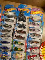 Top down view showing two columns of packaged Hot Wheels vehicles and hard plastic Hot Wheels signs on a wooden floor.