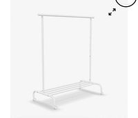 Image of assembled IKEA RIGGA children's clothing rack, showing white metal frame with top hanging bar and lower slatted shelf on caster wheels.