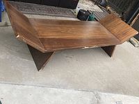 Full view of large solid wood bench outdoors, showing angled ends and surface wear.