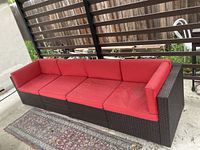 Full view of four-piece wicker sectional sofa with red cushions on concrete patio