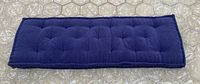 Top-down image of a long, tufted blue seat cushion laid flat on a light carpeted floor.
