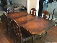 Wood dining table with five matching chairs arranged around it, showing the wood grain and carved details