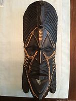 Dark wood African art mask with carved facial features and decorative patterns