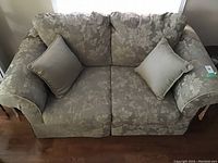 Beige loveseat sofa seen from the front with two matching pillows on each side of the seating area