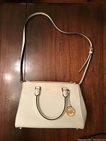 White Michael Kors handbag laid flat showing front with brass logo charm and handles.
