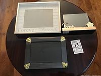 Three picture frames displayed on round wooden table showing size and design details: large 'Forever Friends' white frame, small 'Friends' wooden frame with paw print, black metal frame with gold corners.