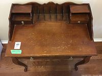 Front and top view of the oak wood secretary desk showing upper compartment with small drawers and pigeonholes, warm brown finish, surface wear visible.