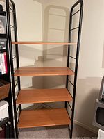 Full view of the shelving unit showing four wood shelves held by black metal side frames with ladder steps for adjustment.