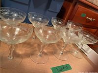 Set of 8 clear champagne coupe glasses with etched floral and leaf design on bowls, displayed on cardboard surface.