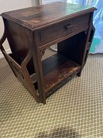 View of antique wooden side table showing single drawer, open shelf, and side magazine compartments with curved wooden side panels.