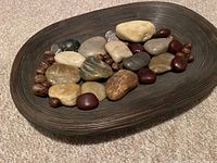 Top view of dark brown oval bamboo tray containing assorted smooth river rocks in various colors along with natural seeds scattered throughout