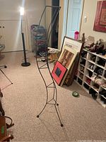 Full length view of the metal three-legged decorative stand placed on the carpeted floor, showing the structure and shape clearly.