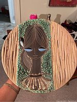 Full view of round decorative wall plate featuring handpainted female face on textured green turquoise and taupe background