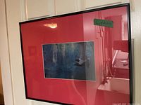 Photo of framed artwork showing red mat and metal black frame with image of lady's legs in strappy heels against blue background.