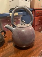 Full side view of the round ceramic tea pot with distinctive handle and spout, glossy soft purple glaze finish.