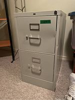 Front view of the white metal filing cabinet showing two drawers with handles and label holders, slight dents visible on the surface.