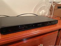 Front view of the black Philips DVD player showing the disc tray, control buttons, and brand name on the front panel.