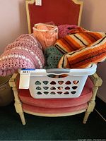 Overall view of the basket filled with multiple afghans placed on a pink upholstered chair.