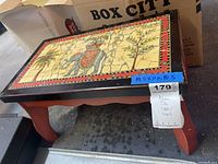 View of the top surface showing Asian-themed decorative tile featuring an elephant and warrior, bordered with red and black trim, and table legs in red paint.