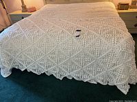 White crochet afghan spread over bed showing diamond pattern and floral clusters, edge scalloped