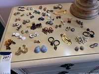Wide view of all costume jewelry earrings arranged on a surface showing diversity in styles, colors, and types including clip-on and pierced earrings.