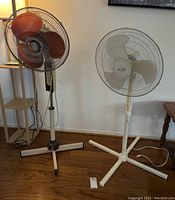 Photo showing two floor fans standing side by side; one with brown blades and another with white blades