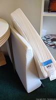 Two foam wedge pillows leaned against a white shelf and a table, showing their angled shape and white covers.