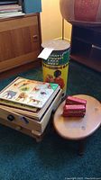 Wide shot showing Lincoln Logs container, puzzles on wooden box, vintage wooden stool with die cast buses on top.