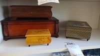 Four wooden boxes on shelf: dark large box, yellow box, patterned box, medium music box