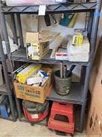 Photo showing plastic shelving rack with Dry Vac vacuum cleaner Model 338.179200 on bottom shelf, several boxes of light bulbs and other items scattered on middle shelves, a red step stool next to vacuum, and decorative container with metal pipes.