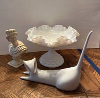 Photo showing all three items: porcelain cat figurine, hobnail milk glass candy dish, and small bust sculpture on a wooden surface with a plain background.