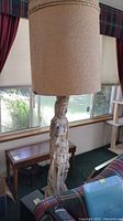 Full lamp view showing beige drum lampshade and tall figure base in living room setting.